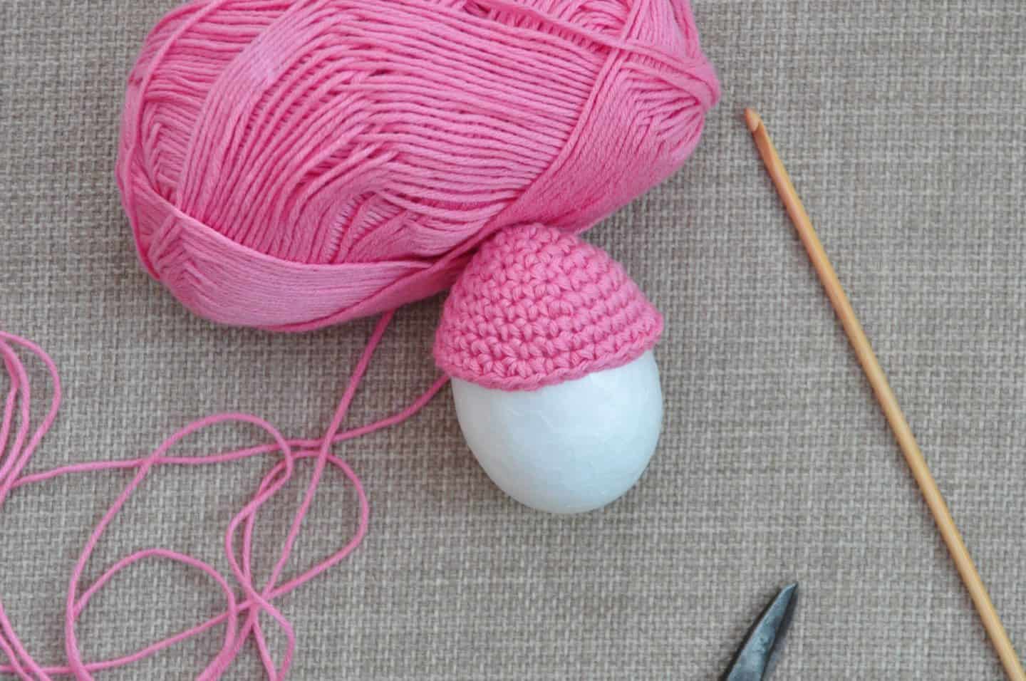 crochet Easter egg pattern being put on polystyrene egg with pink yarn in background