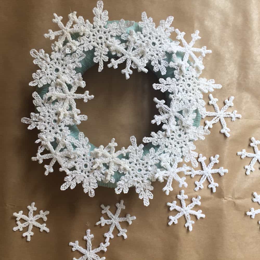 Finished crochet snowflake wreath laying on some brown parchment paper.