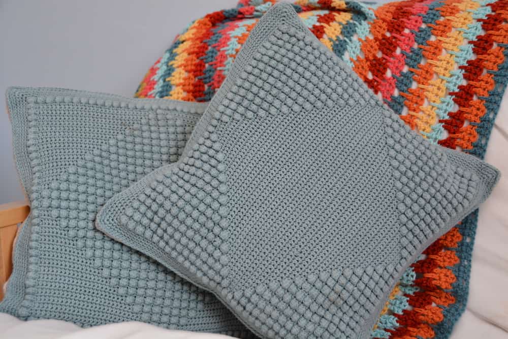 bobble stitch crochet cushion pattern - two cushions sitting in front of colourful crochet blanket