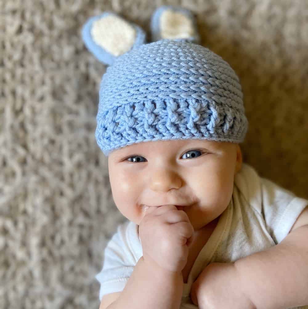 smiling baby wearing crochet bunny hat with floppy ears.