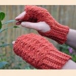 A beginner crocheter is holding a pair of fingerless mitts.