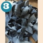 A pile of blue denim strips on a table with a crochet pattern.