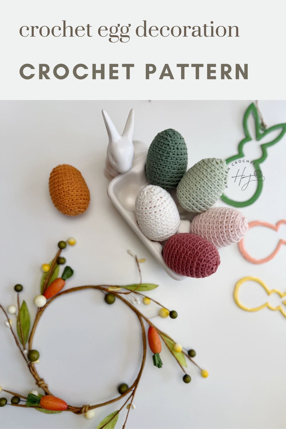 Five crochet Easter eggs in various colors are displayed in a white bunny-shaped egg holder, with decorative items and a floral wreath nearby. Text reads: "crochet egg decoration CROCHET PATTERN".