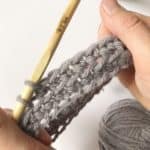 A person creating a crochet pattern using a wooden stick.