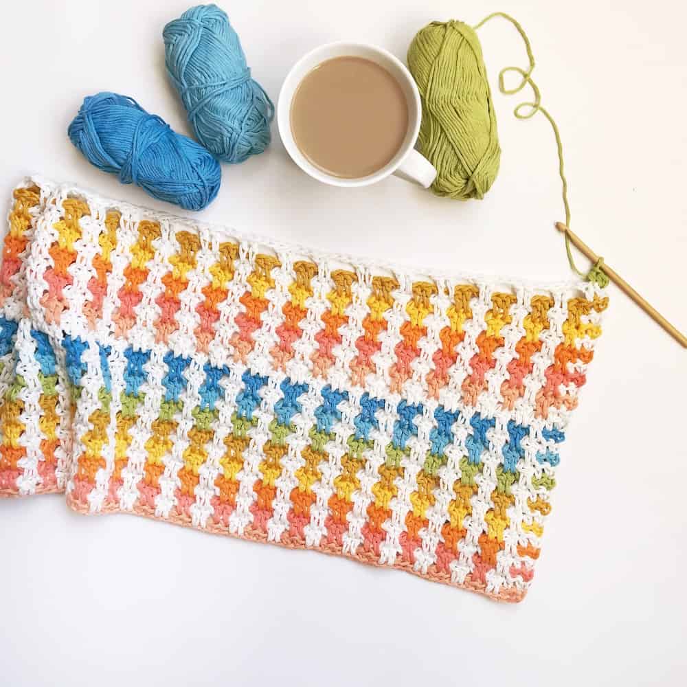 crochet poncho in progress laid out on table with crochet hook, bright yarn and a cup of tea