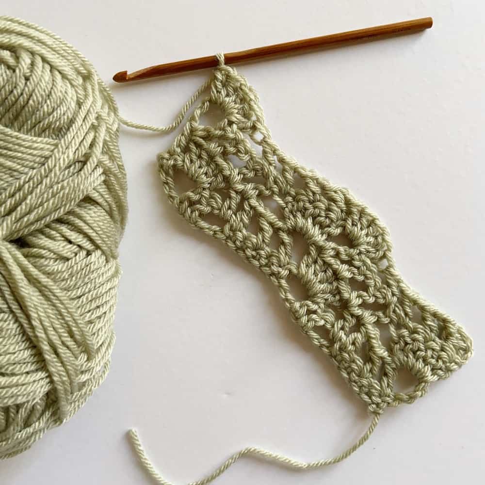 lacy wave crochet stitch in light green yarn with wooden crochet hook
