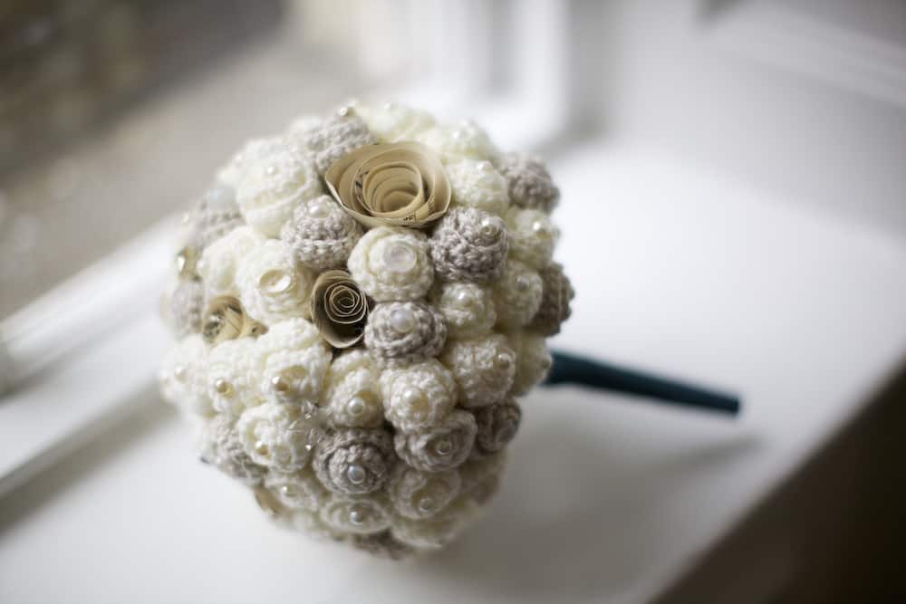 Close up of handmade crochet wedding bouquet with cream and ivory flowers, pearly beads, vintage buttons and brooches.