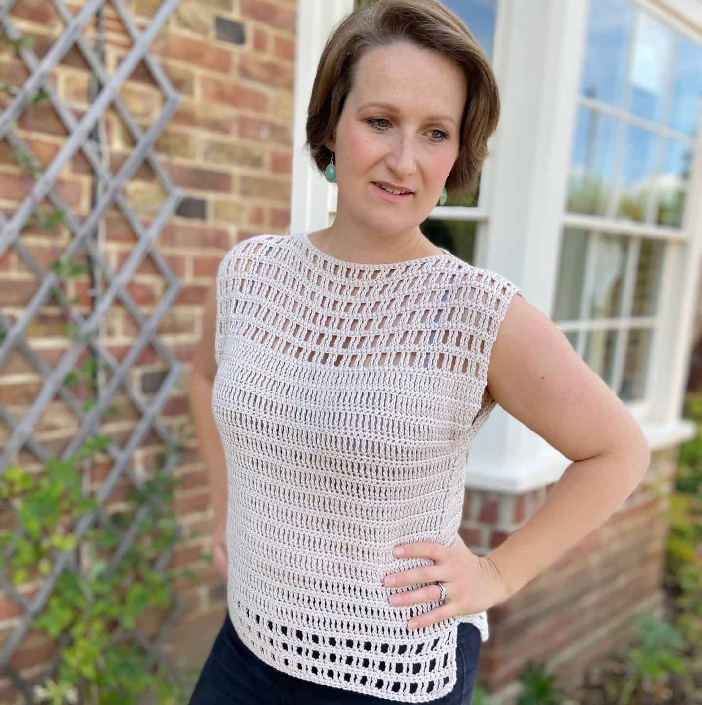 Woman in garden wearing cream-colored crochet lace top and green earrings.