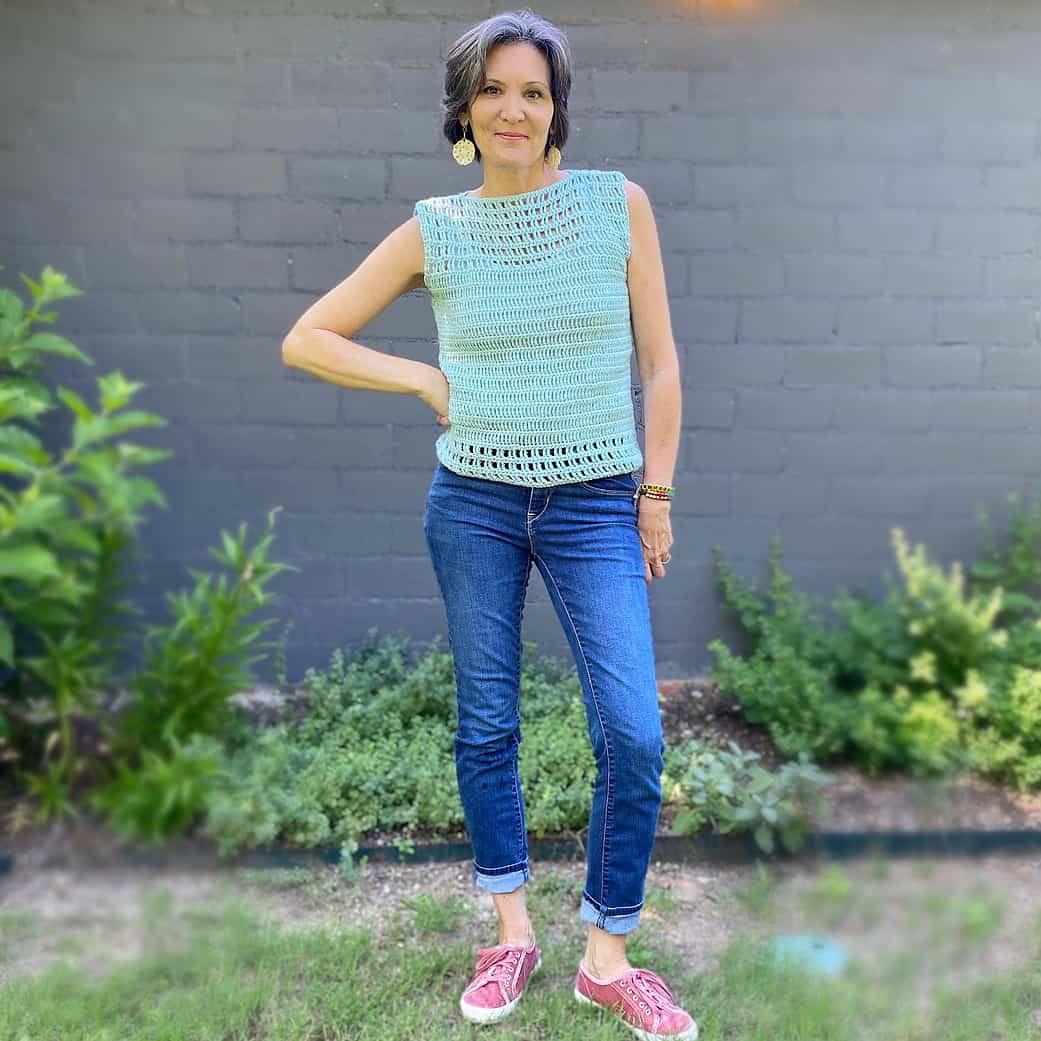 Woman in green crochet summer top standing in front of grey brick wall.