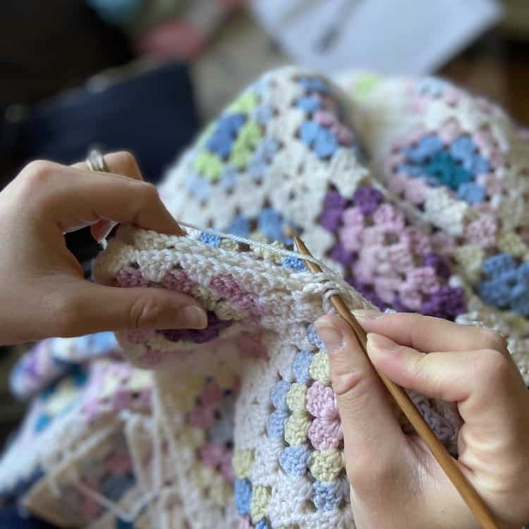 Closeup of two hands working a seam of a crochet blanket.