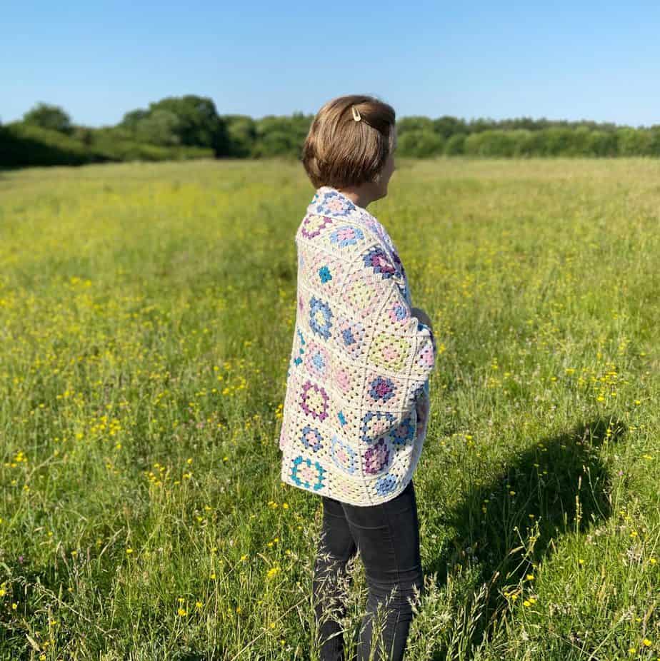 Woman in field wearing granny square blanket cardigan.