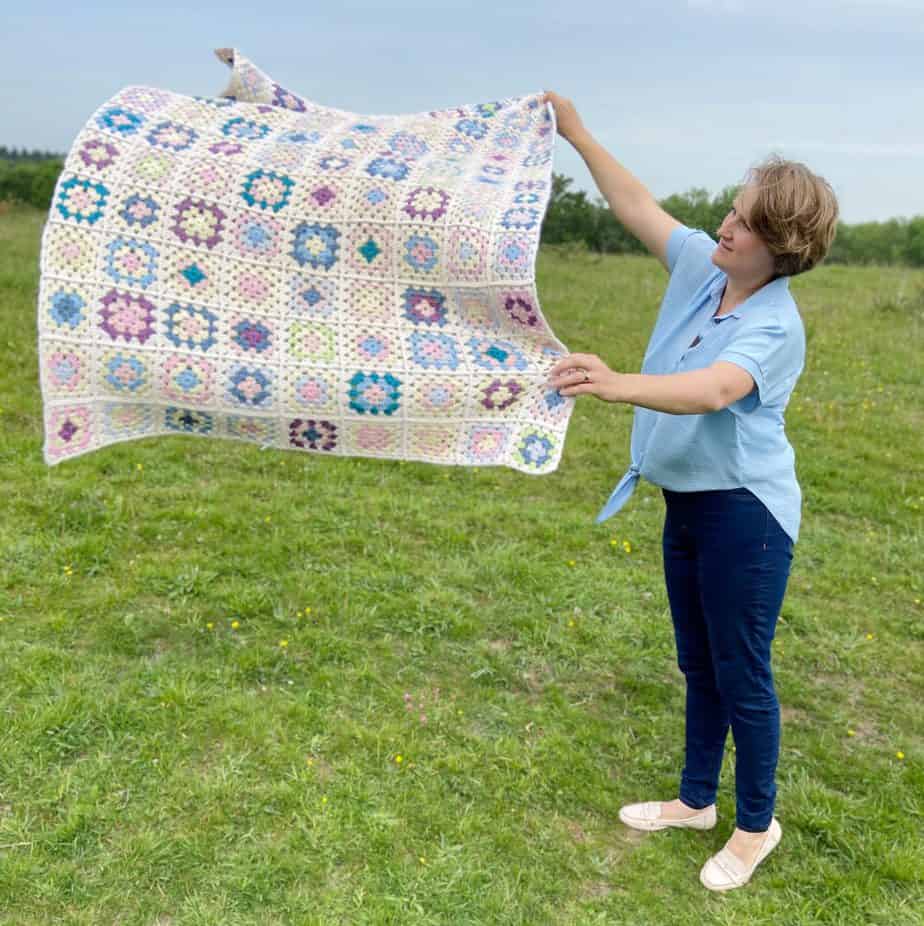 Woman in field throwing a granny square crochet blanket in the air.