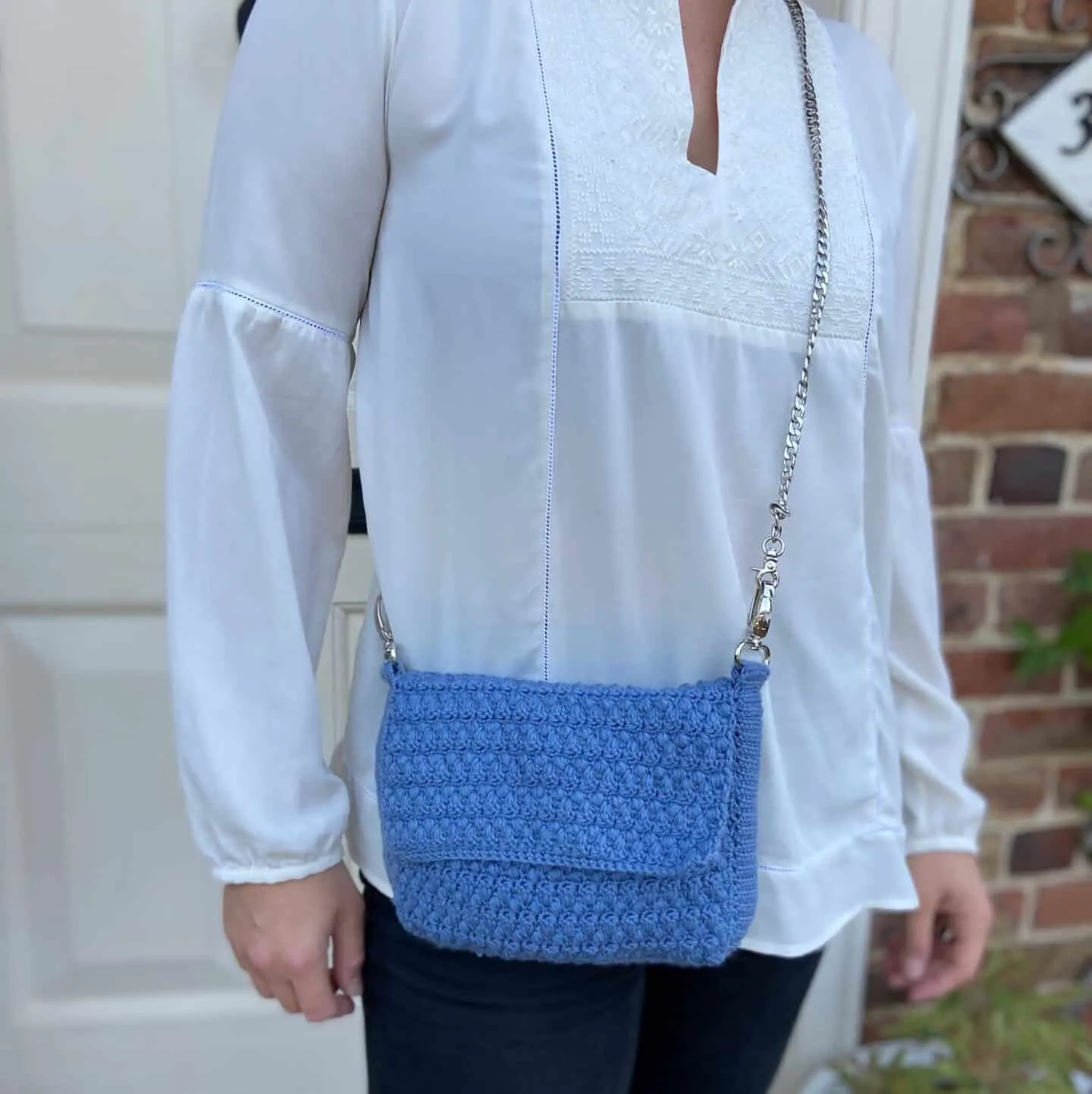 Blue crochet shoulder bag on woman in white shirt.