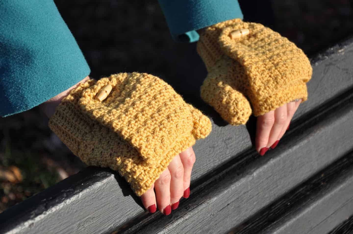 woman wearing mustard yellow crochet fingerless gloves leaning on a bench