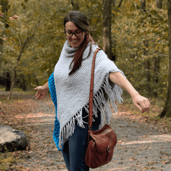 woman in woods wearing grey crochet poncho and leather handbag