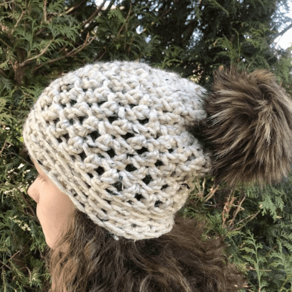 woman looking sideways wearing chunky grey crochet bobble hat