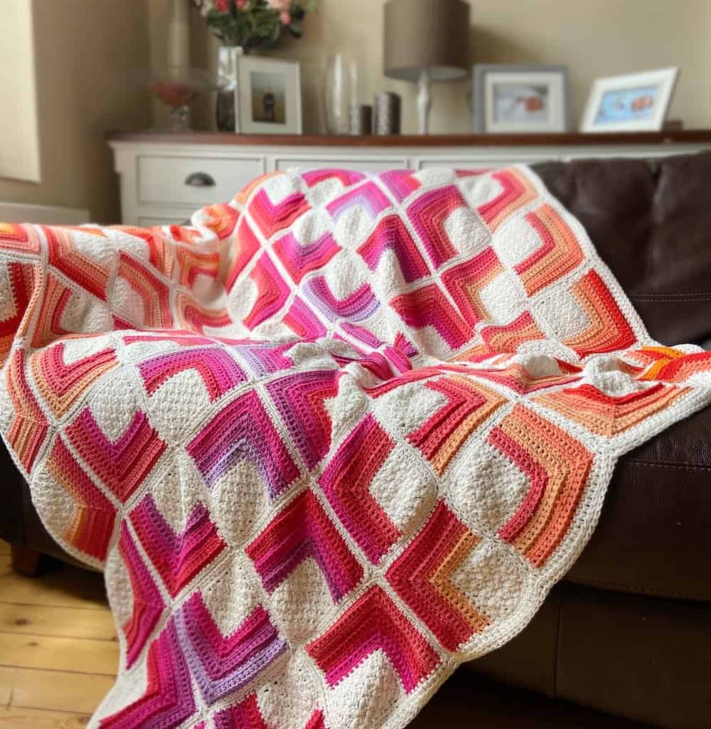 ombre crochet square motif blanket in bright colours laid on sofa