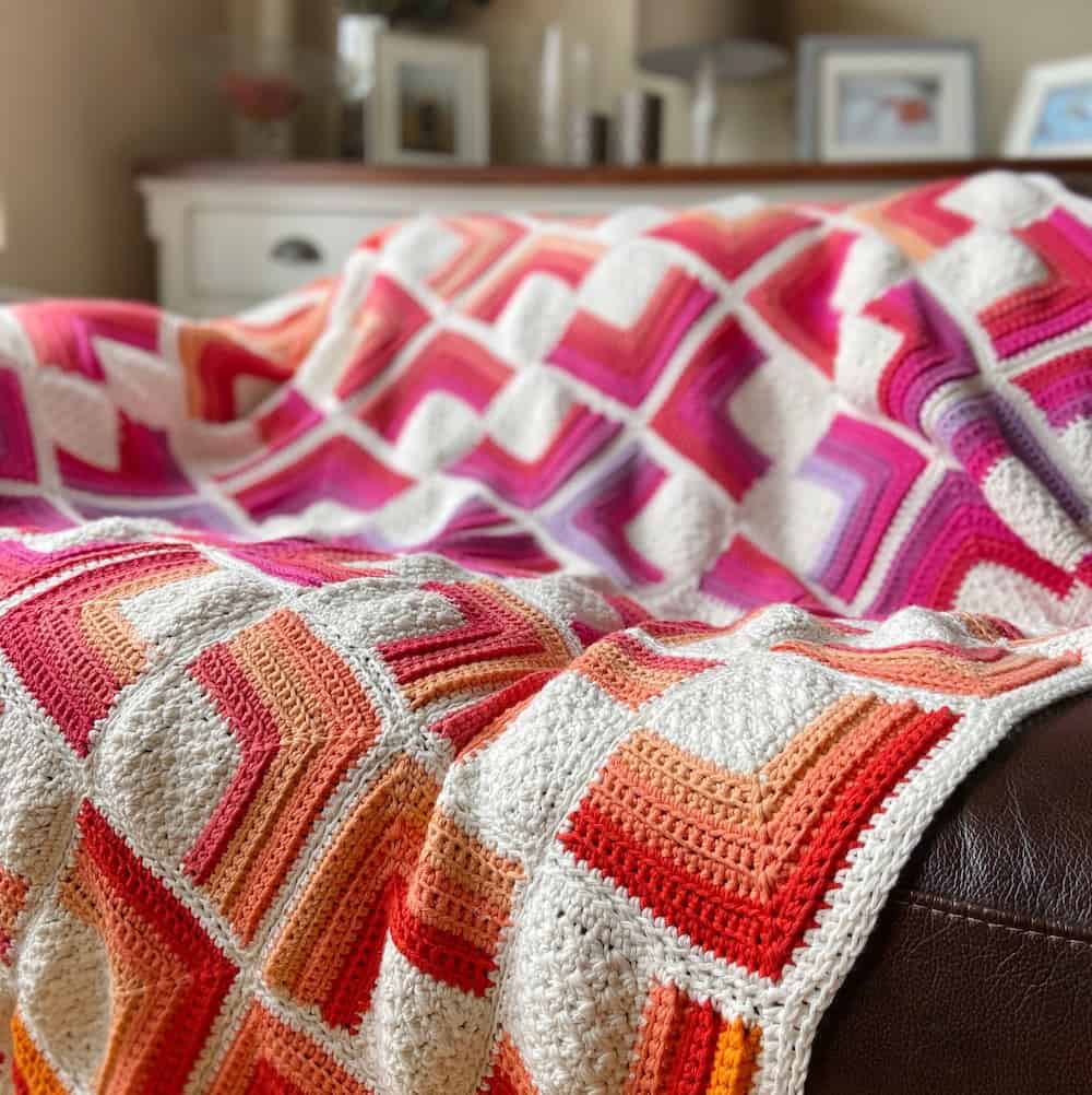 red, orange, yellow, pink and white crochet square motif blanket on brown leather sofa