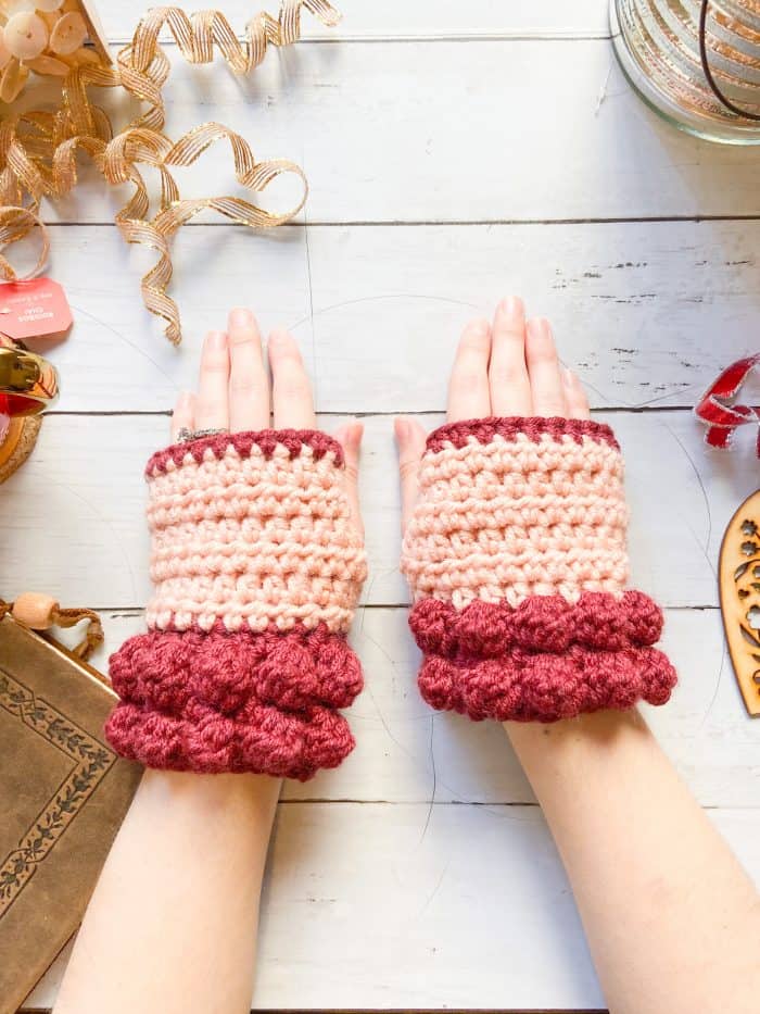 woman wearing chunky red bobble crochet fingerless mitts laid on table with gold Christmas trimmings 