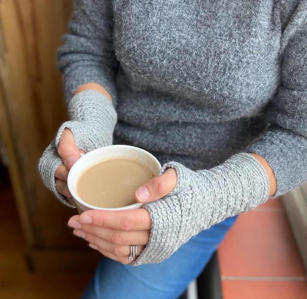 image of woman's hands holding coffee cup wearing modern grey crochet gloves
