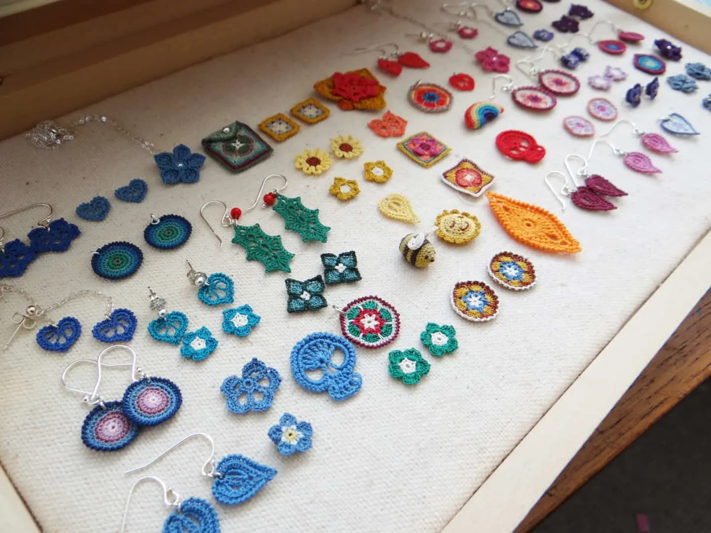 micro crochet earrings and motifs laid out in wooden presentation box, including holly leaves, granny squares, tiny flowers, skulls, bumble bees and more