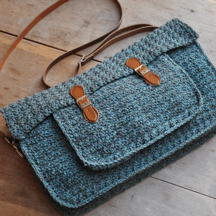 blue tweed messenger satchel bag with brown leather straps on wooden table