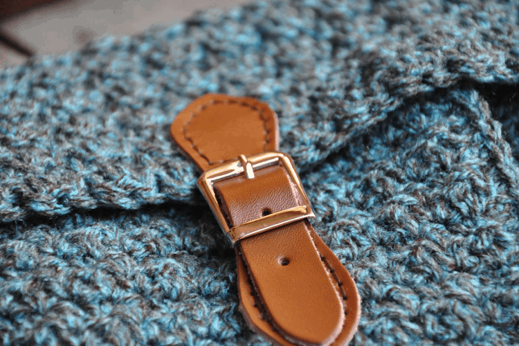 close up of brown leather buckle strap on crochet messenger bag laying on wooden table