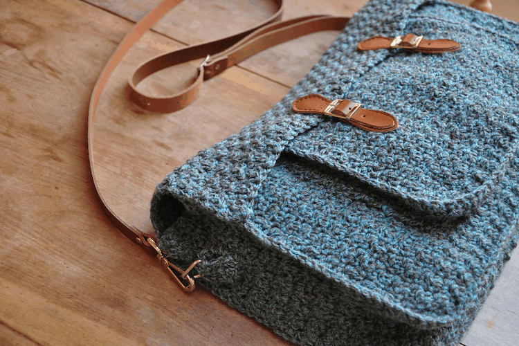 Quotidian Crochet Satchel a messenger bag with brown leather straps in crochet laying on wooden table