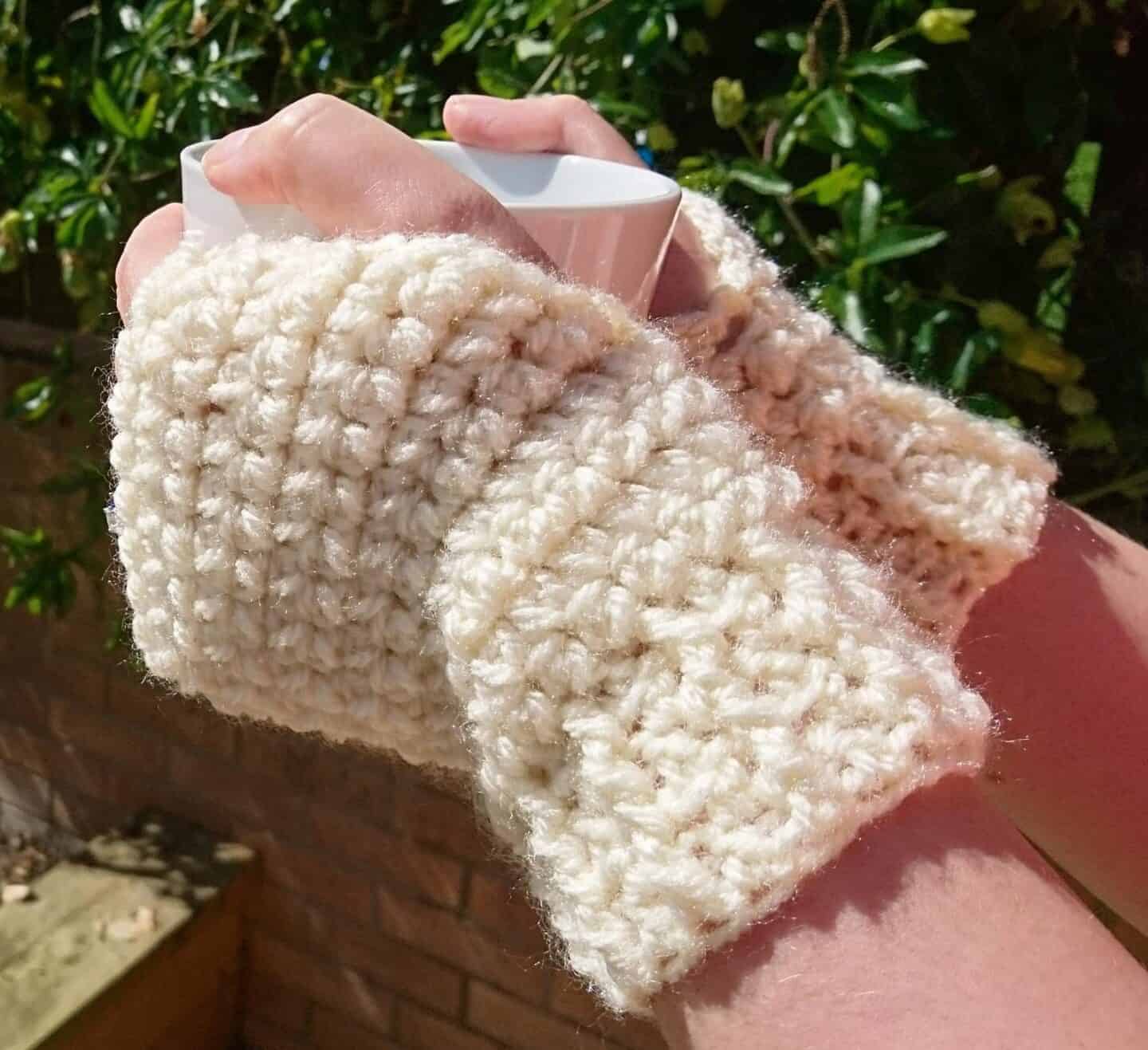 cream crochet wrist warmers holding cup of coffee