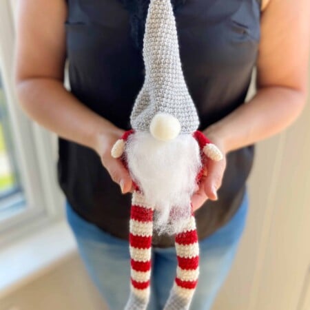 Christmas crochet gnome in red, white and grey being held by woman in hands