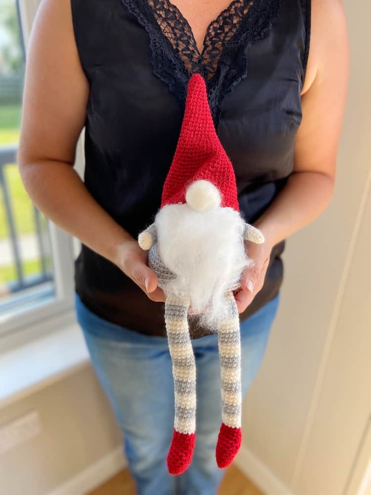 Woman holding Christmas crochet gnome with red hat and grey and white stripe legs.