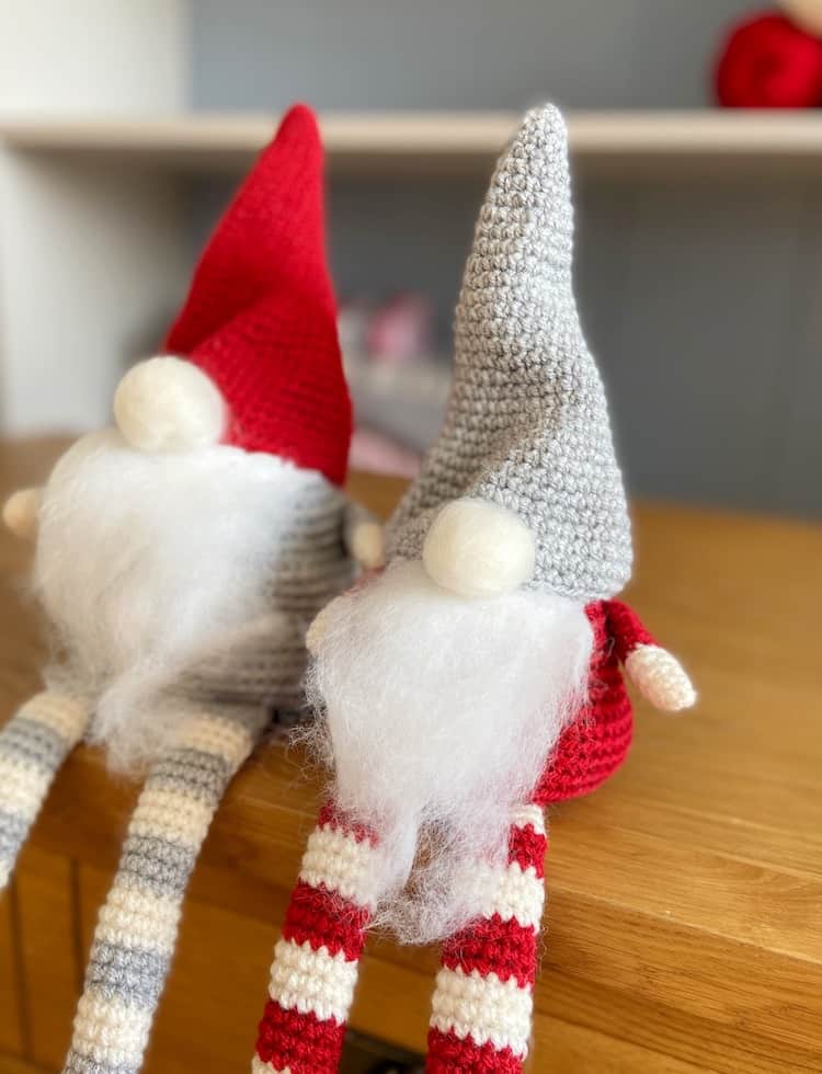 Pair of red, white and grey Christmas crochet gnomes sitting on table.
