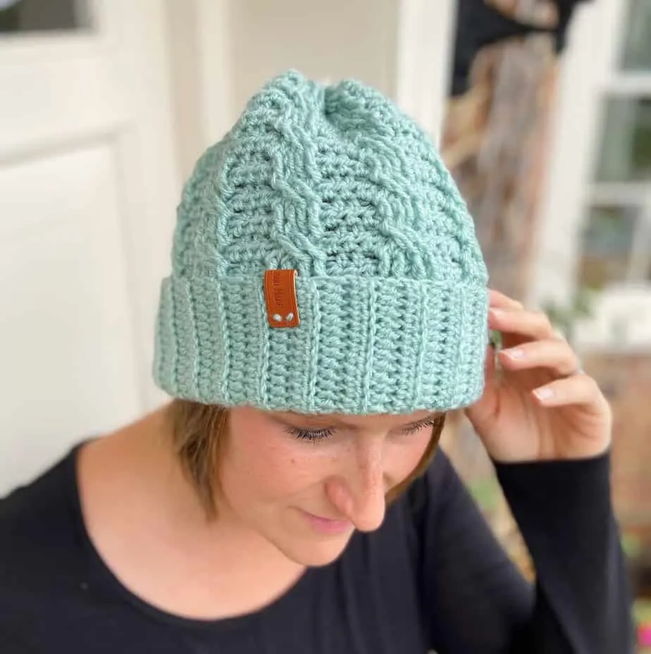 Woman wearing mint green crochet cable hat touching the brim with her fingers.