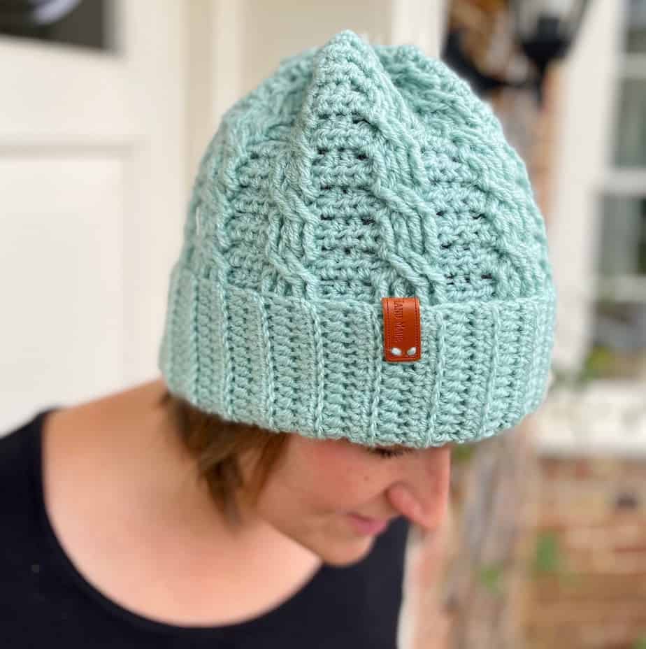 Woman looking down, wearing mint green crochet cable hat.