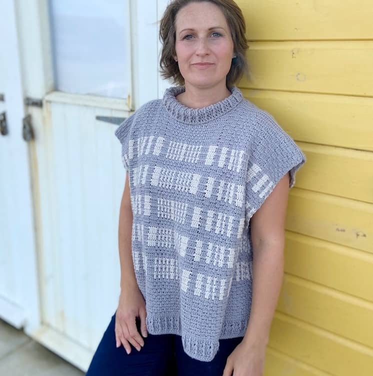 woman leaning against beach hut wearing grey and white stripe crochet poncho