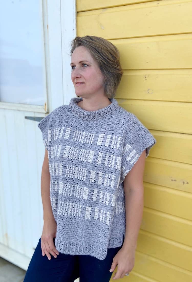 woman leaning against beach hut wearing grey crochet poncho