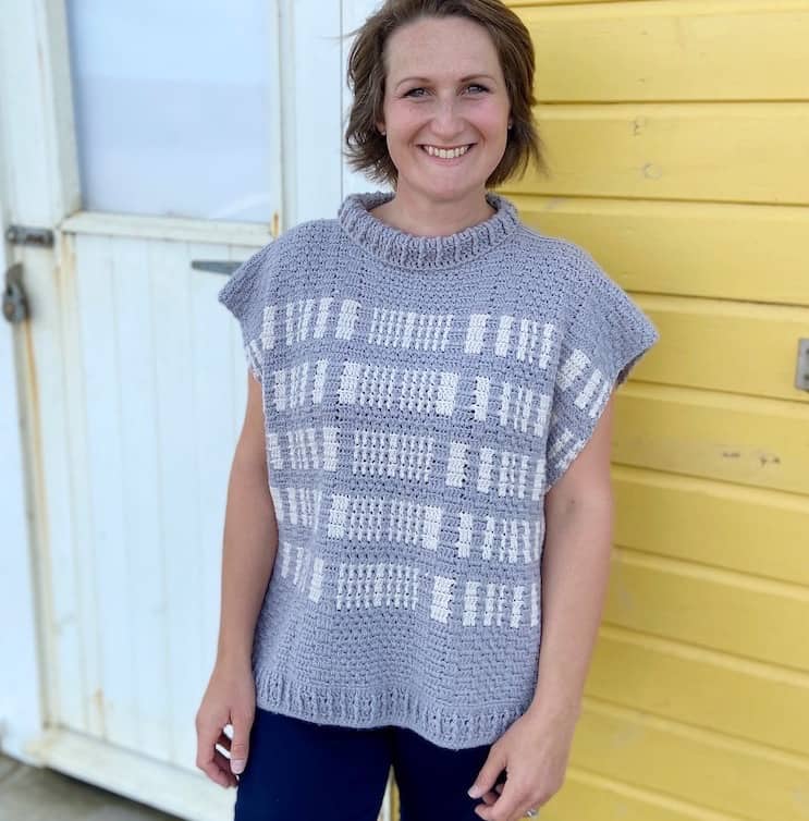 woman smiling straight at camera wearing grey and white roll neck crochet poncho 