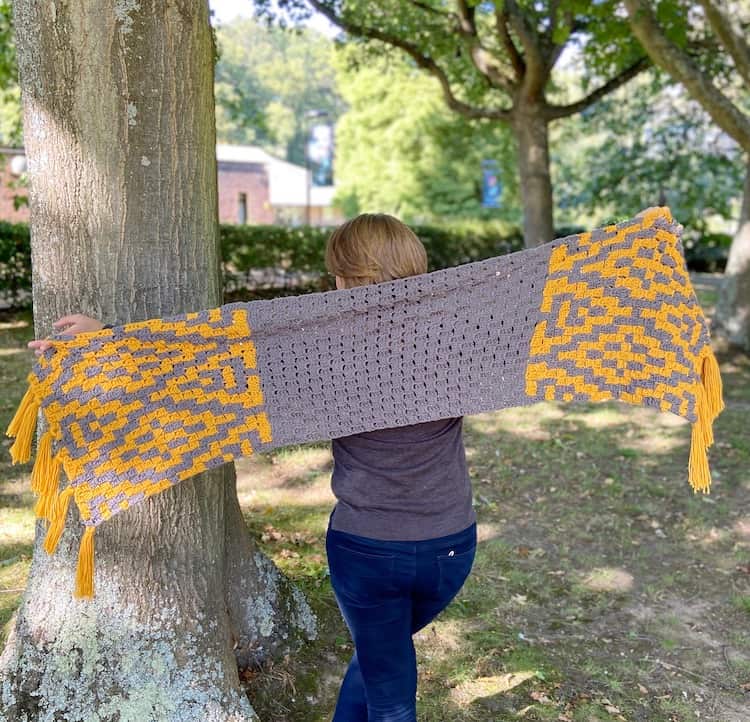 woman by trees holding a c2c crochet winter scarf stretched out