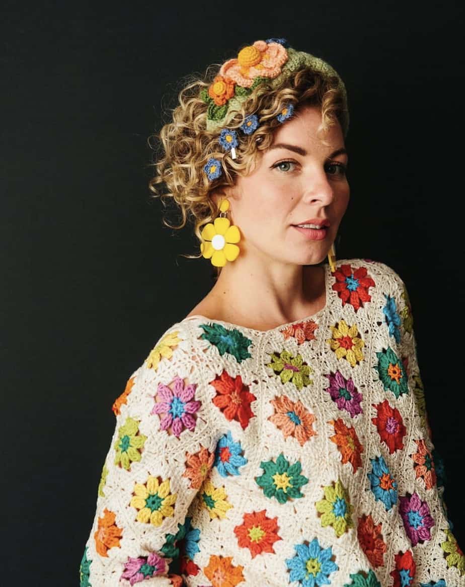 Woman wearing bright flower motif crochet jumper and large yellow daisy earrings.