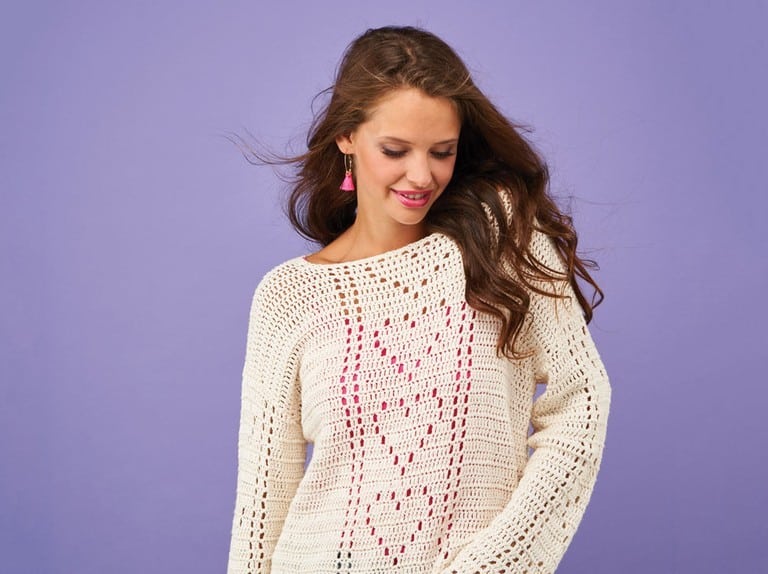 Woman with long hair wearing cream filet crochet jumper with hearts on it.