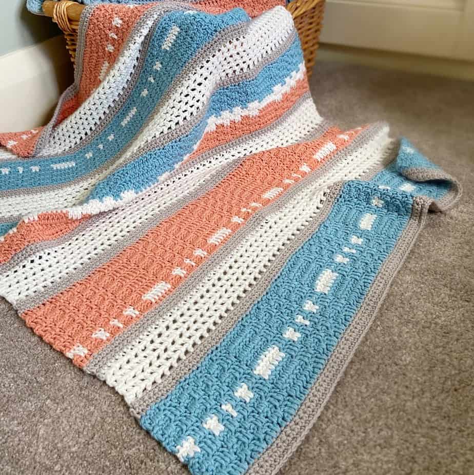 Modern peach and teal crochet baby blanket draped over a basket on the floor.