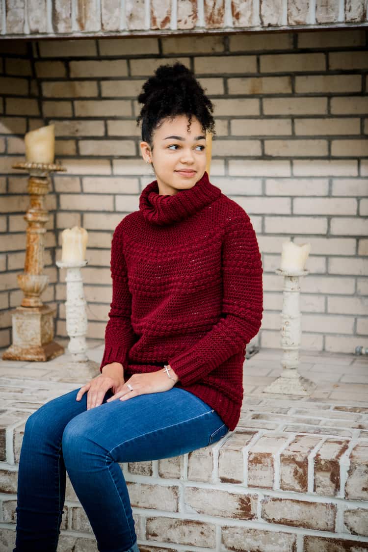 woman sitting wearing cranberry biscotti turtleneck crochet foundry sweater