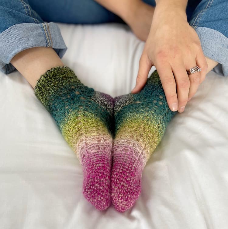 ombre lacy crochet socks being worn with feet together and hand holding ankle