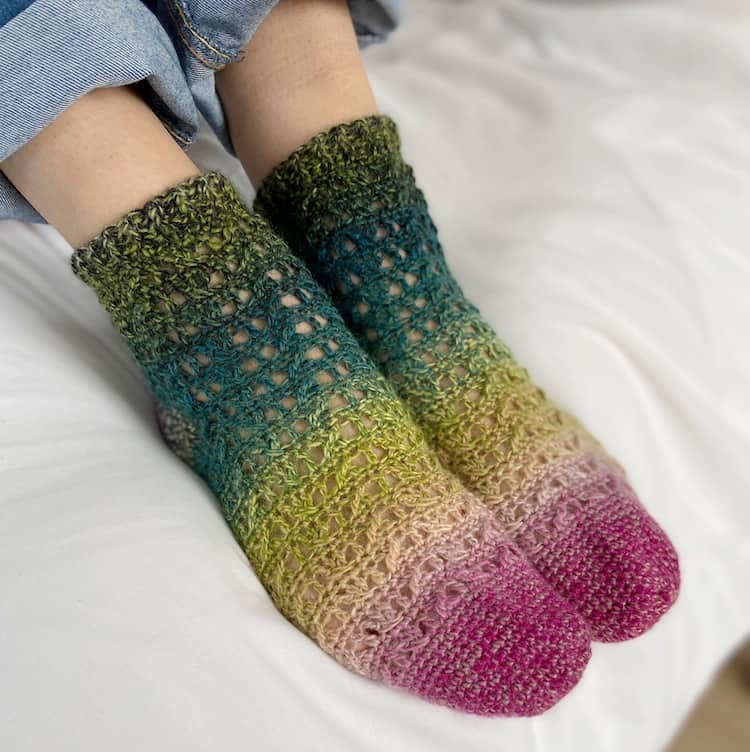 feet wearing ombro crochet socks with toes pointing down and denim jeans