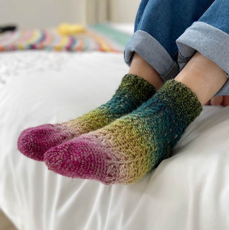 pink and green lacy crochet socks being worn by woman sitting on bed