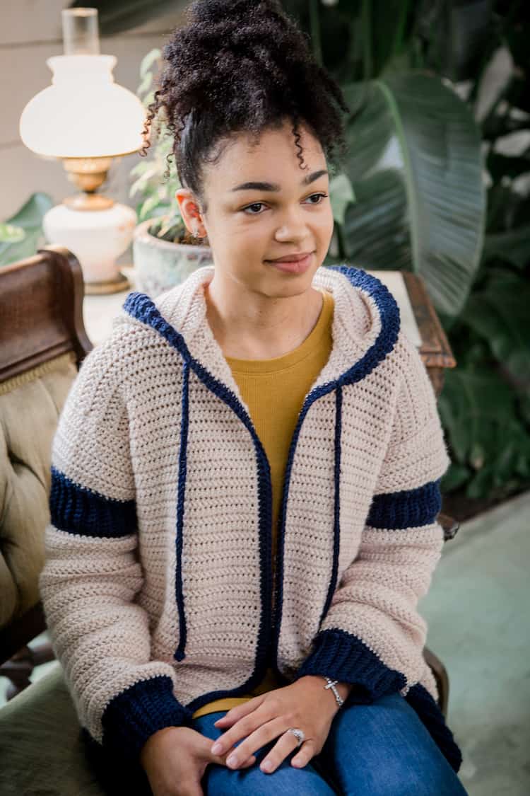 woman sitting wearing pizelle crochet hooded cardigan in cream and navy