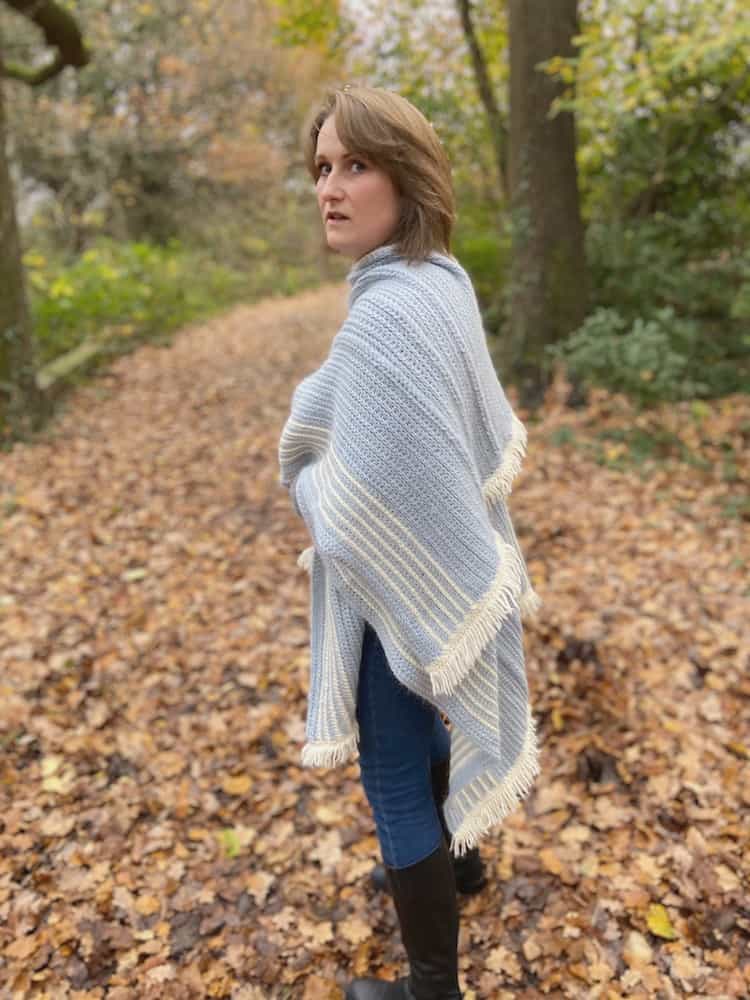 Woman looking back over her shoulder in woodland wearing braided blanket crochet ruana.