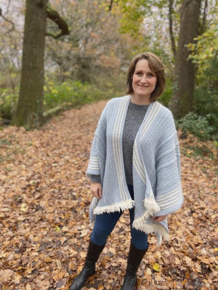 Smiling woman in woods wearing light blue crochet ruana wrap.