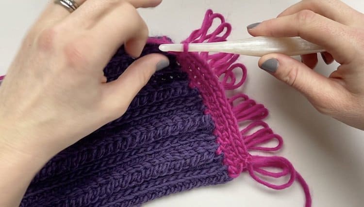 hands crocheting a loop stitch fringe in chunky pink yarn