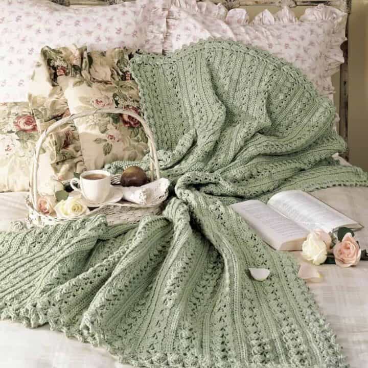 Green crochet afghan laying on a bed.